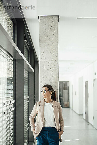 Thoughtful businesswoman with eyeglasses standing at office