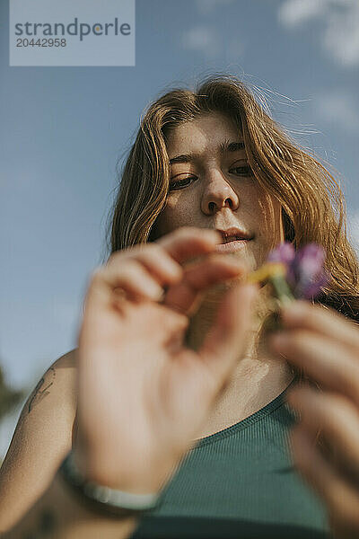 Woman examining flowers in front of sky