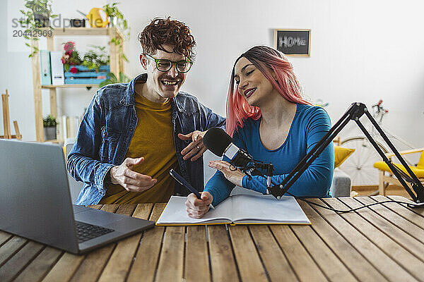 Smiling influencers filming live podcast with laptop and microphone at home