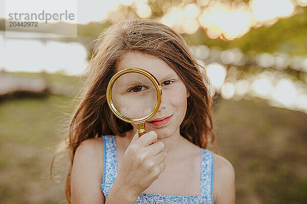 Redhead girl looking through with magnifying glass at garden