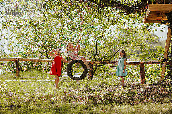 Cheerful girls playing with tire swing at garden