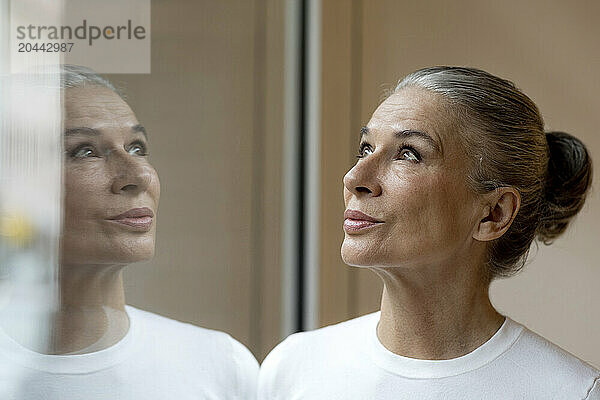 Senior gray haired woman with reflection on window