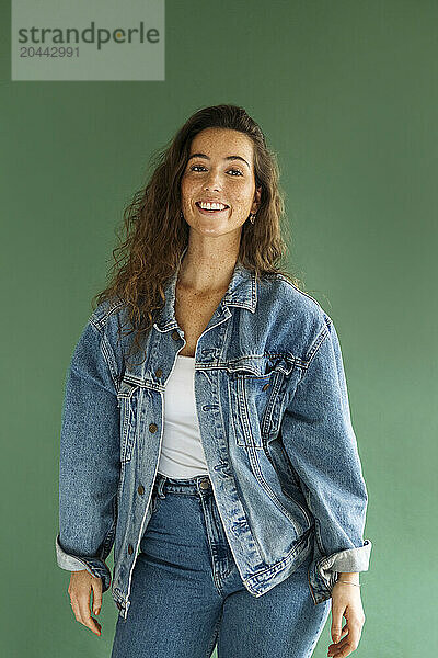 Smiling woman in denim jacket standing against green background