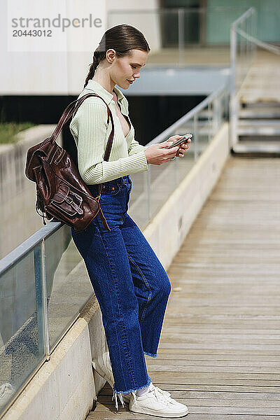 Woman leaning on railing and using smartphone