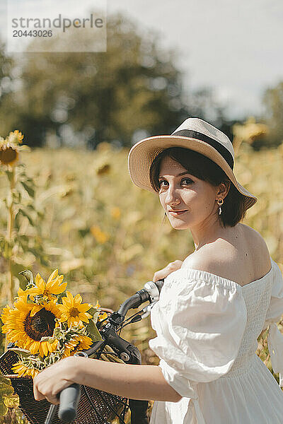 Young woman with sunflower in bicycle basket at field