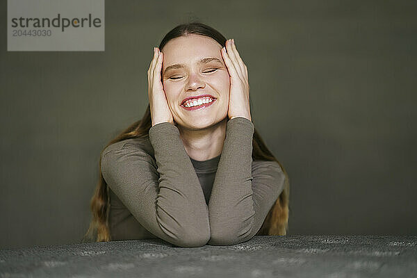 Cheerful woman sitting at table in front of gray wall