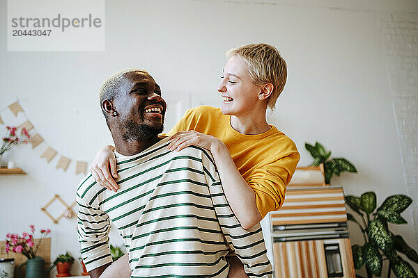 Happy young man piggybacking girlfriend at home