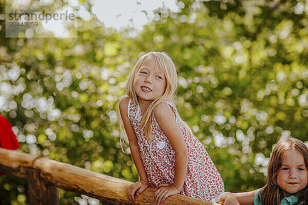 Smiling blond girl on fence by friend at garden