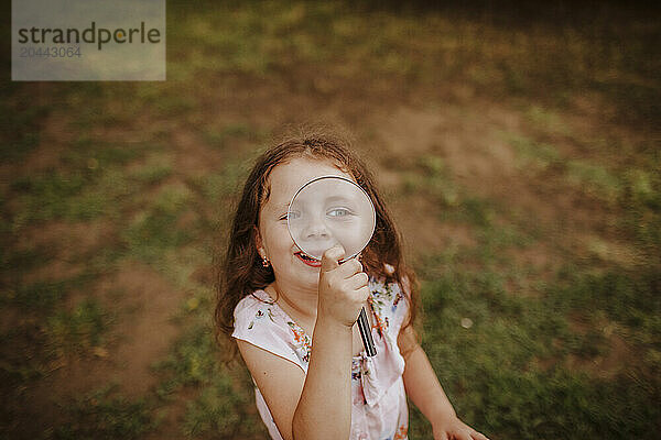 Cute smiling girl looking through with magnifying glass