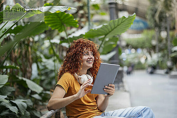 Smiling redhead young woman with curly hair using tablet PC