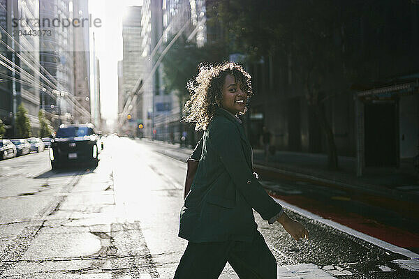 Happy young businesswoman crossing street in city