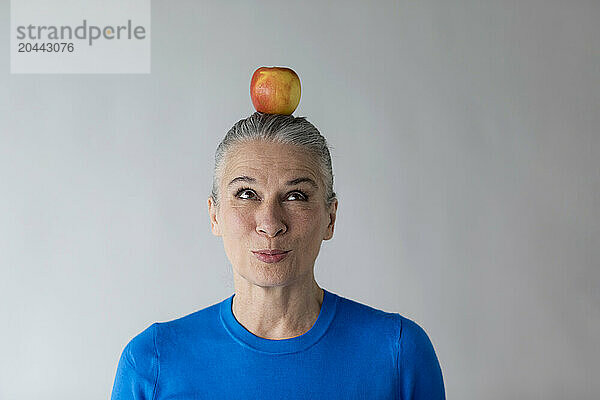 Senior woman balancing apple on head in front of wall