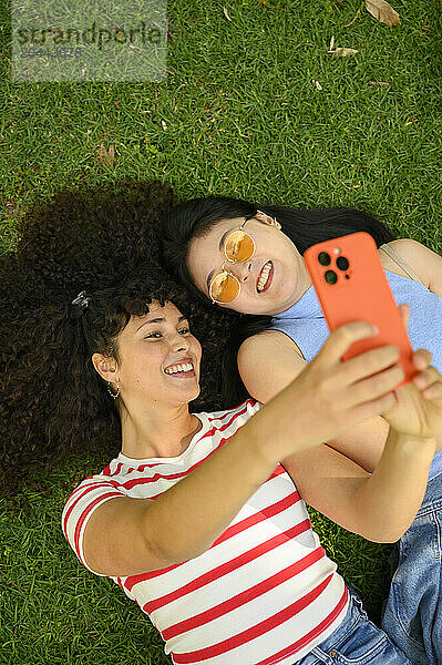 Smiling friends taking selfie and lying on grass at park