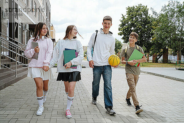 Smiling teenage boys and girls walking together at schoolyard