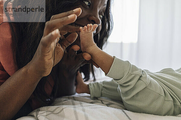 Mother touching daughter's feet lying on bed at home