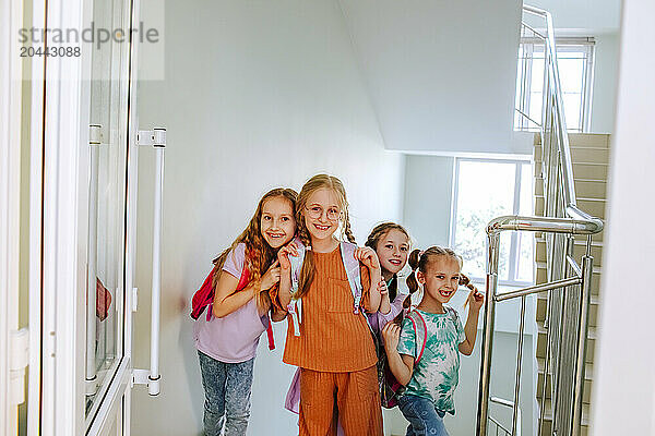 Cheerful schoolgirls with backpack standing at school staircase