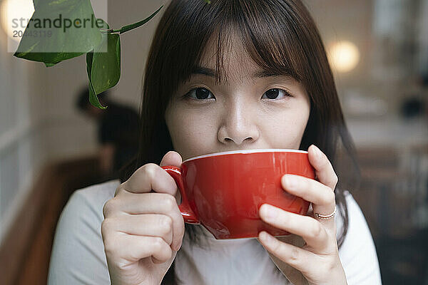 Young woman drinking coffee in red cup at cafe