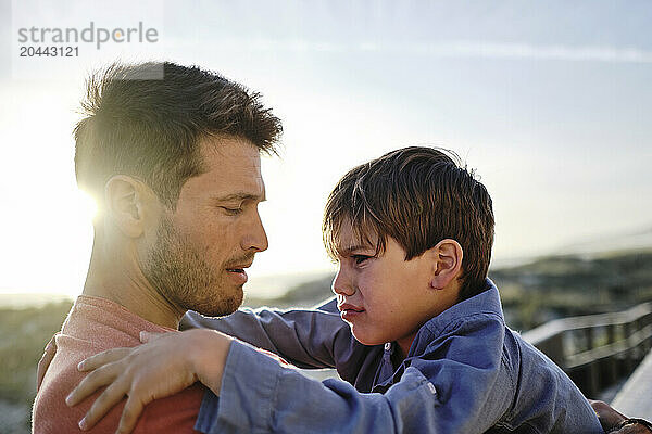 Father comforting crying son at beach