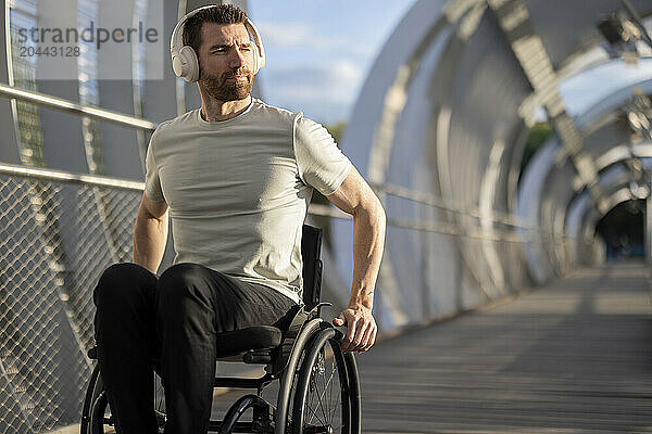 Man with disability enjoying music through wireless headphone and sitting on wheelchair at bridge