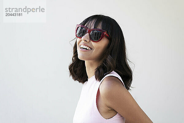 Happy young woman wearing sunglasses in front of white wall