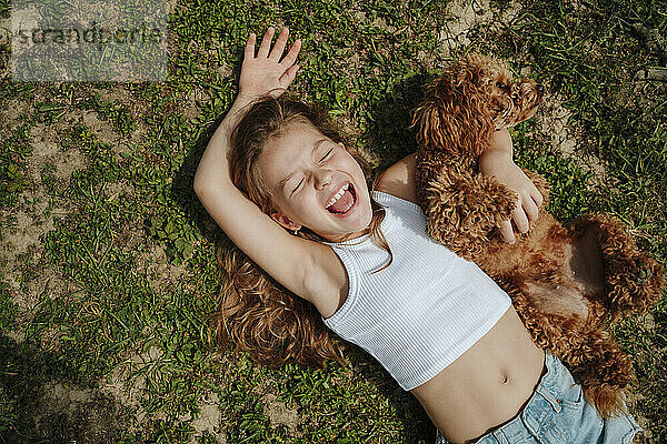 Girl and Maltipoo dog lying on grass at farm