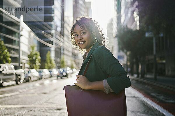 Smiling businesswoman with purse crossing street in city