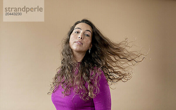 Woman tossing hair against beige backdrop