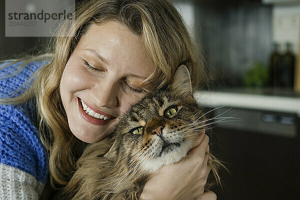 Happy woman embracing cat at home