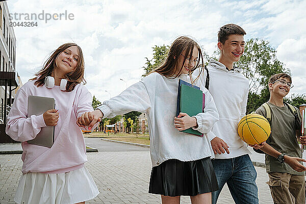 Smiling teenage girls and boys walking together at schoolyard