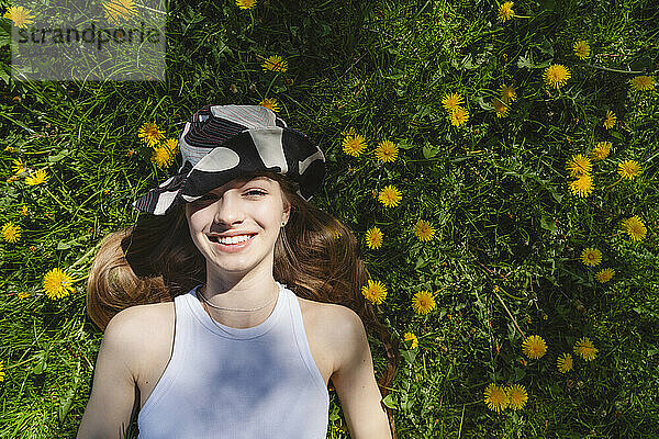 Happy girl wearing hat and lying on yellow dandelions