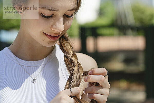 Smiling teenage girl tying braid on sunny day