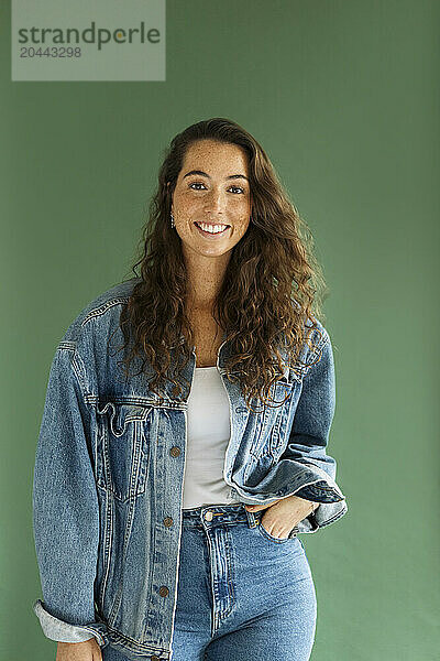 Smiling woman with hand in pocket standing against green background