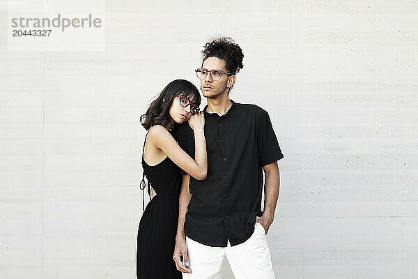 Young woman leaning on man shoulder standing in front of white wall