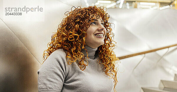 Smiling beautiful redhead young woman with curly hair looking up