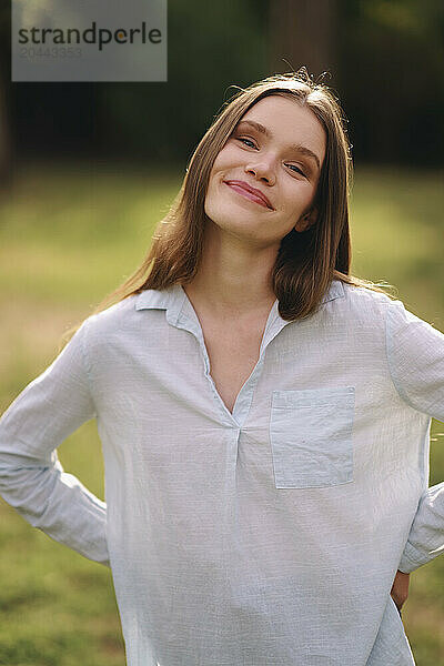 Smiling woman with hand on hip standing at field