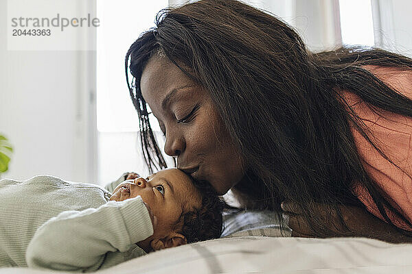 Mother kissing daughter forehead lying on bed at home