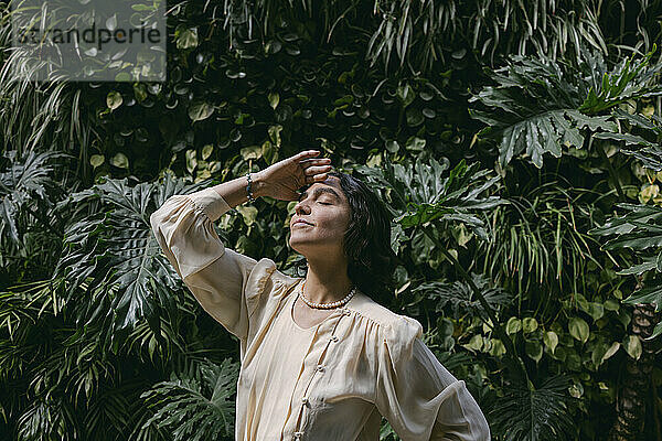 Smiling woman standing in front of plants on sunny day