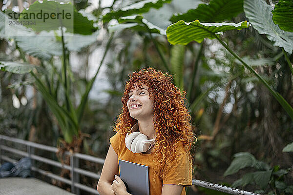 Smiling redhead young woman day dreaming with tablet PC