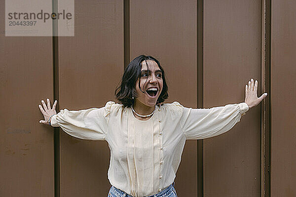 Cheerful woman standing in front of brown wall