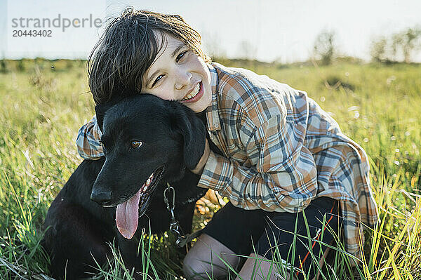 Smiling boy hugging dog on grass