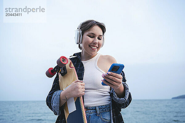 Young woman with skateboard using mobile phone listening to music