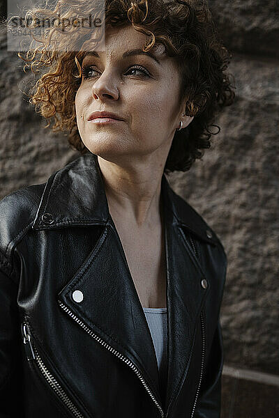 Thoughtful woman with curly hair standing near wall