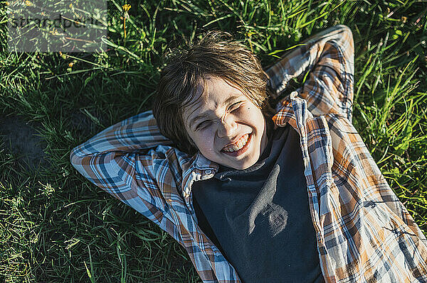 Smiling boy with hands behind head lying on grass