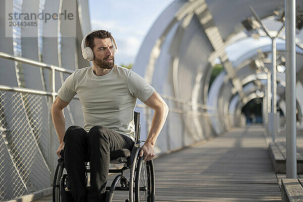 Man with disability listening music through wireless headphone and sitting on wheelchair at bridge