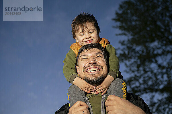 Happy father carrying son on shoulders at park