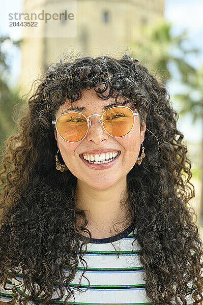 Smiling woman with curly hair wearing yellow sunglasses