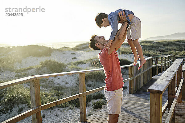 Father carrying son on boardwalk at beach