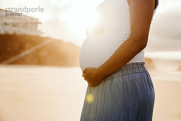 Pregnant woman with hands on stomach at sunset