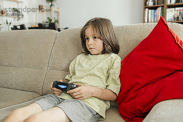 Cute boy sitting on sofa and playing video game at home