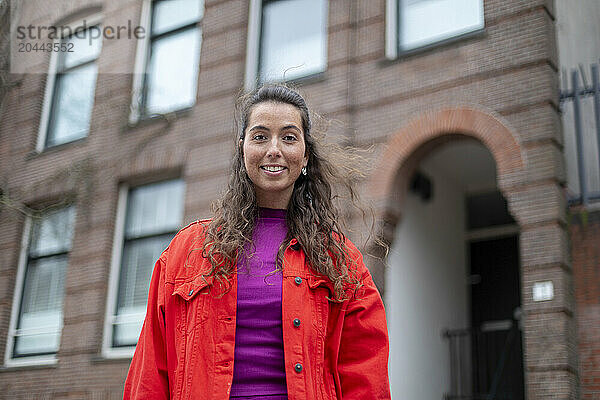 Smiling woman in red jacket standing in front of building